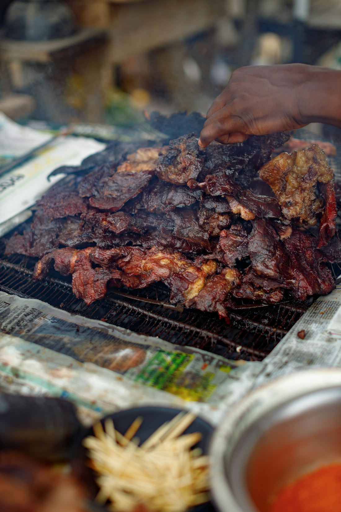 A hand flips grilled meat over an open fire.