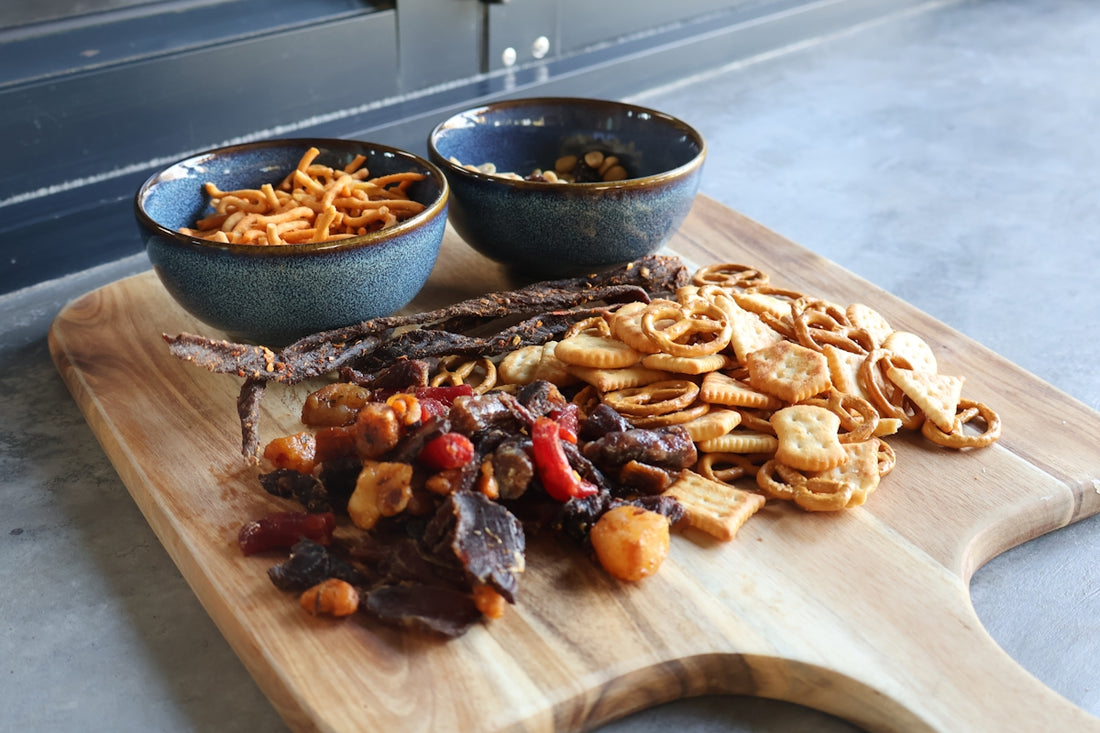 Assorted snacks and dried fruits on a wooden board.
