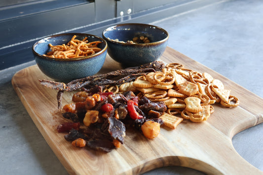 Assorted snacks and dried fruits on a wooden board.